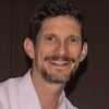 Headshot of Jeffrey Drope, a smiling man with brown hair, a moustache and goutee, wearing a pink collared shirt posed against a dark backdrop