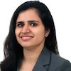 Headshot of Kritika Khanijo, a smiling woman with long, dark hair, wearing a grey suit, and posed against a white backdrop