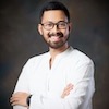 Headshot of Gumilang Aryo Sahadewo, a smiling man with dark hair, eyeglasses, wearing a white shirt and posed against a dark backdrop