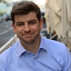 Headshot of Kevin Welding, a smiling man with brown hair, wearing a light blue collared shirt, posed against an outdoor backdrop
