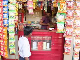 A young consumer gazes at a cigarette advertising poster displayed at eye-level at a convenience market stand in India