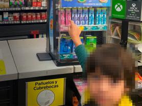 A child with their face blurred reaches their outstretched arm towards a countertop tobacco product display at a retailer in Mexico