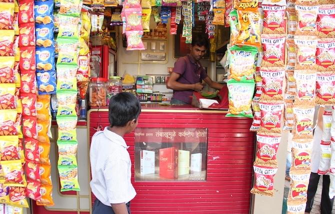 A young consumer gazes at a cigarette advertising poster displayed at eye-level at a convenience market stand in India