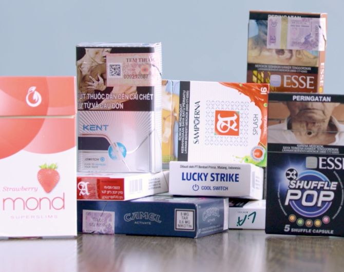 An array of colorful, flavored cigarette packs purchased in Indonesia, Vietnam, and the Philippines, arranged on a tabletop with a grey background